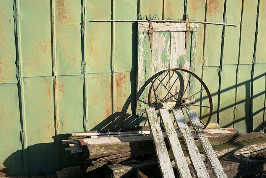 woodpile, wagon wheel against weathered green shed wall